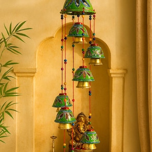 Peut inclure: Un carillon suspendu avec des accents verts, bleus et rouges. Le carillon présente des ornements en forme de cloche avec des motifs floraux et des cloches dorées. Le carillon est suspendu devant une statue dorée d'une divinité.