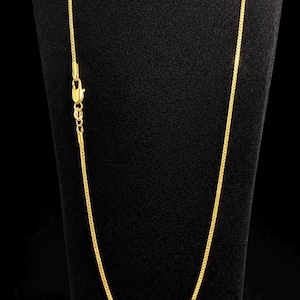 Puede incluir: Un collar de cadena de color dorado con un diseño delicado de eslabones cuadrados uniformes. El collar se asegura con un pequeño cierre de mosquetón funcional situado en el lado izquierdo, ofreciendo un acabado metálico consistente en toda la pieza.