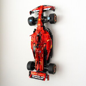 Könnte beinhalten: Ein rotes und schwarzes Formel-1-Rennwagenmodell mit Sponsorenlogos und schwarzen Reifen. Das Modell ist an einer weißen Wand montiert und zeigt sein aerodynamisches Design und seine komplizierten Details. Das Auto ist etwa 50 cm lang.