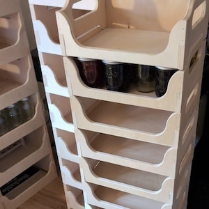 Puede incluir: Estanterías de almacenamiento apilables de madera clara con múltiples compartimentos. Las estanterías están diseñadas para contener tarros. Algunas estanterías contienen tarros de vidrio con varios contenidos. El diseño permite apilar y organizar fácilmente.