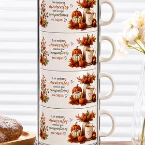Puede incluir: Un juego de cuatro tazas de cerámica blanca apiladas verticalmente en un soporte de metal cromado. Cada taza presenta un diseño otoñal con calabazas, hojas y el texto: Los mejores momentos son los que compartimos en casa.