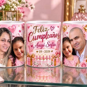 May include: A white ceramic mug featuring a pink birthday theme with gold and pink heart balloons, a cake with candles, and gift boxes. The text reads Feliz Cumplea&ntilde;os, Anyi Sofia, 09-2026, and Que siempre brilles. The mug displays two different family photos.
