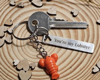 May include: A silver key with a keychain that reads "You're my Lobster." The keychain has an orange lobster charm. The key and keychain are on a wooden surface with small wooden hearts.