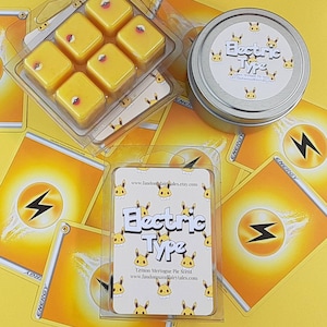 May include: A set of six yellow wax melts in a clear plastic container. The wax melts are shaped like squares and have a small red circle in the center of each square. The container is surrounded by yellow and white playing cards with the word "ENERGY" printed on them. The container also has a label that says "Electric Type" and "Lemon Meringue Pie Scent".