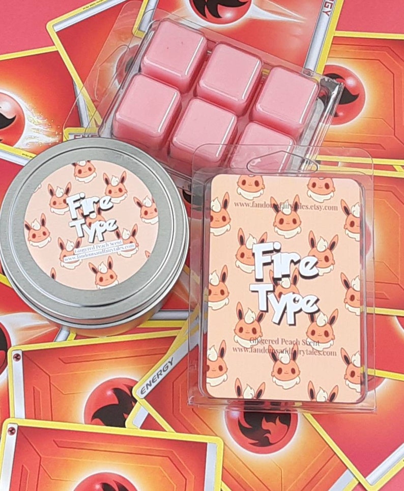 May include: A set of six pink wax melts in a clear plastic container. The wax melts are shaped like squares and are arranged in a grid pattern. The container is labeled with the text "Fire Type" and a website address. The wax melts are surrounded by Pokemon trading cards with a fire theme.