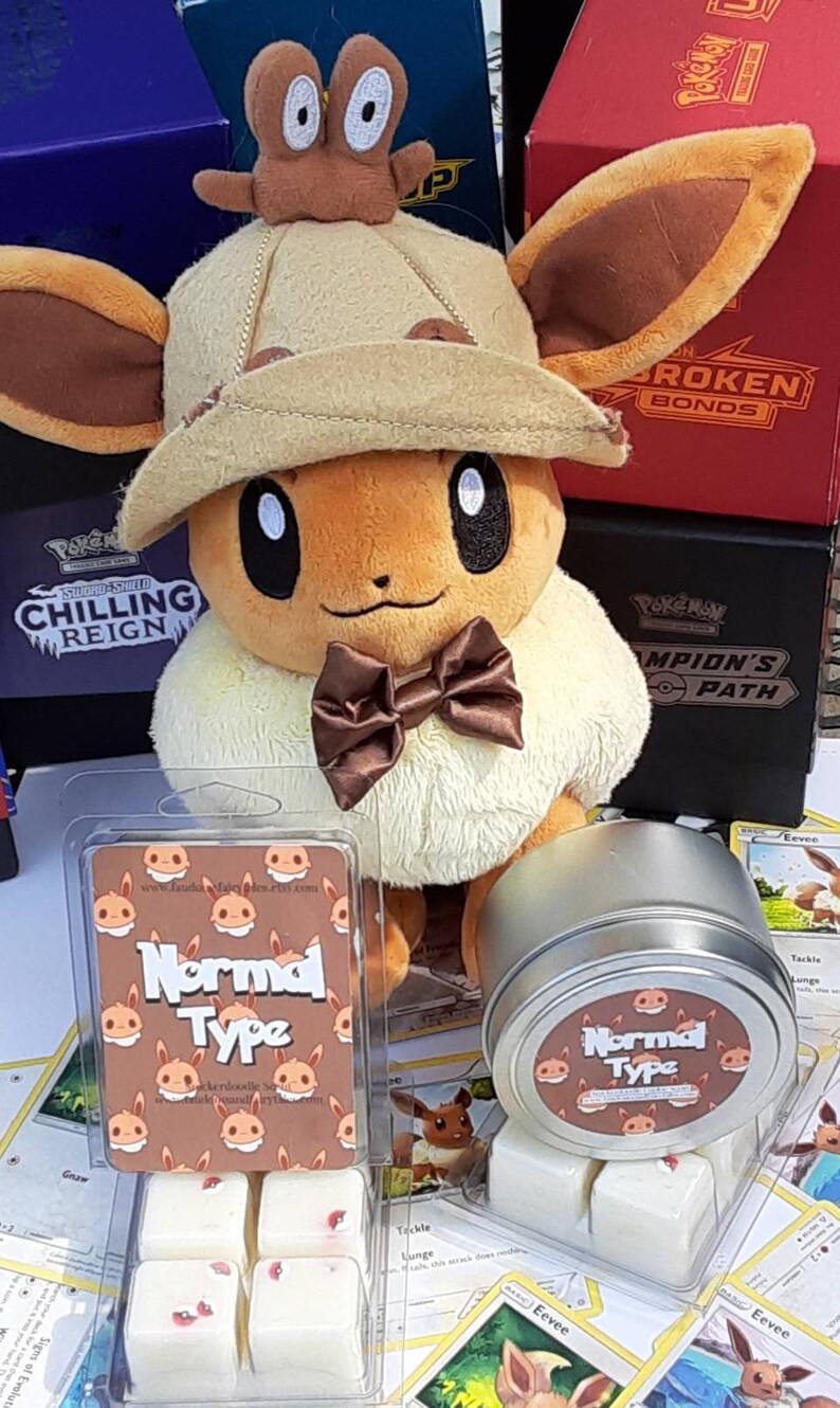 May include: A brown and tan Eevee plush toy wearing a brown hat with a small brown Eevee plush toy on top. The Eevee plush toy is wearing a brown bow tie. The Eevee plush toy is sitting on a table with a clear plastic container of wax melts and a metal tin of wax melts. The wax melts are labeled "Normal Type".