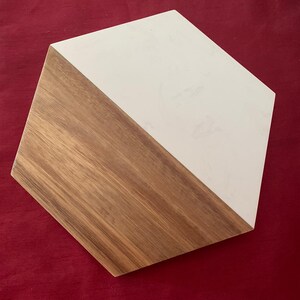 May include: A hexagonal wooden coaster with a diagonal split design. One half is natural wood grain, the other is white. The coaster is set against a red background.