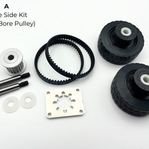 May include: A Drive Side Kit with a 6mm Bore Pulley. The kit includes two black rubber wheels, two black belts, a silver pulley, two bolts, two washers, and a silver mounting plate. The text "A" is in the upper left corner.