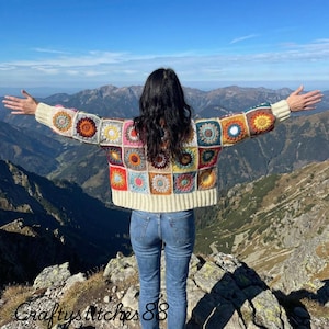 May include: A long-sleeve crochet cardigan constructed from multicoloured granny squares featuring circular floral patterns in shades of red, yellow, blue, and orange, finished with cream-coloured ribbed cuffs and a matching ribbed hemline.