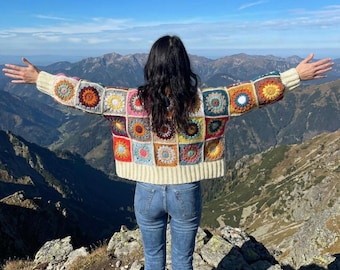 May include: A long-sleeve crochet cardigan constructed from multicolored granny squares featuring circular floral patterns in shades of red, yellow, blue, and orange, finished with cream-colored ribbed cuffs and a matching ribbed hemline.