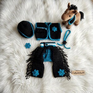 Peut inclure: Un ensemble au crochet pour cheval en peluche comprenant un gilet noir et turquoise, des jambi&egrave;res &agrave; franges noires, un chapeau, un petit accessoire de cou et deux ornements en forme de fleur. Un petit cheval en peluche marron est inclus.