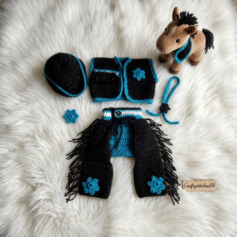 Peut inclure: Un ensemble au crochet pour cheval en peluche comprenant un gilet noir et turquoise, des jambi&egrave;res &agrave; franges noires, un chapeau, un petit accessoire de cou et deux ornements en forme de fleur. Un petit cheval en peluche marron est inclus.