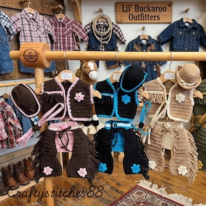 Peut inclure: Trois ensembles de tenues de cow-boy au crochet, comprenant chacun un gilet, des jambi&egrave;res et un chapeau. Les ensembles sont marron avec des accents roses, noirs avec des accents bleus et beige avec des accents blancs. Chaque gilet a une &eacute;toile.