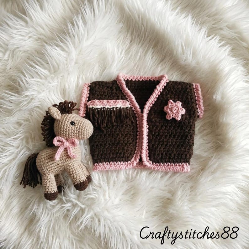 Peut inclure: Un gilet au crochet marron avec des bordures roses, une frange et une applique en forme d'&eacute;toile rose, accompagn&eacute; d'un petit cheval au crochet beige avec une crini&egrave;re, une queue et des sabots marron fonc&eacute;, orn&eacute; d'un n&oelig;ud rose. Texte : CraftyStitches88.