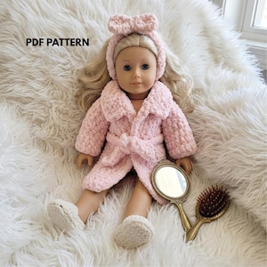 May include: A doll with blonde hair wearing a light pink crocheted robe, matching slippers, and a headband with a bow. The doll is accompanied by a small gold-toned hand mirror and a hairbrush. The text PDF PATTERN is visible in the upper left.