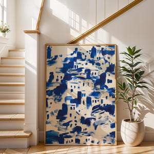 a large blue and white abstract painting displayed on a wall, with a potted plant and a staircase visible in the background.