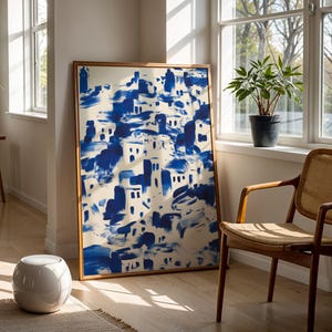 a large blue and white abstract painting displayed on a wall, with a wooden chair and a potted plant nearby.