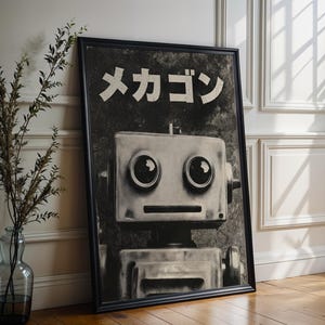 A framed black and white photograph of a robot with large eyes and a textured face, placed on a wooden floor next to a vase with greenery.