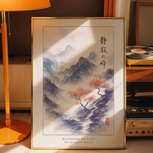 A framed print of a Japanese landscape with mountains and cherry blossoms is displayed on a wooden surface, accompanied by a lamp and a record player.