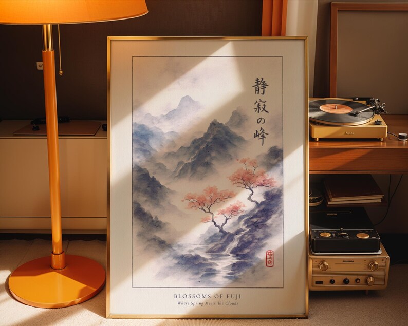 A framed print of a Japanese landscape with mountains and cherry blossoms is displayed on a wooden surface, accompanied by a lamp and a record player.