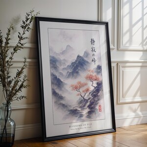 a framed painting of a serene landscape with mountains, trees, and a stream, placed on a wooden floor next to a vase with greenery.
