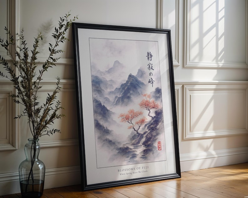 a framed painting of a serene landscape with mountains, trees, and a stream, placed on a wooden floor next to a vase with greenery.