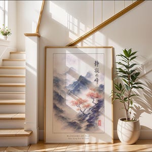 a large framed painting of a serene landscape with mountains, trees, and a winding path, placed on a wall near a staircase and a potted plant.