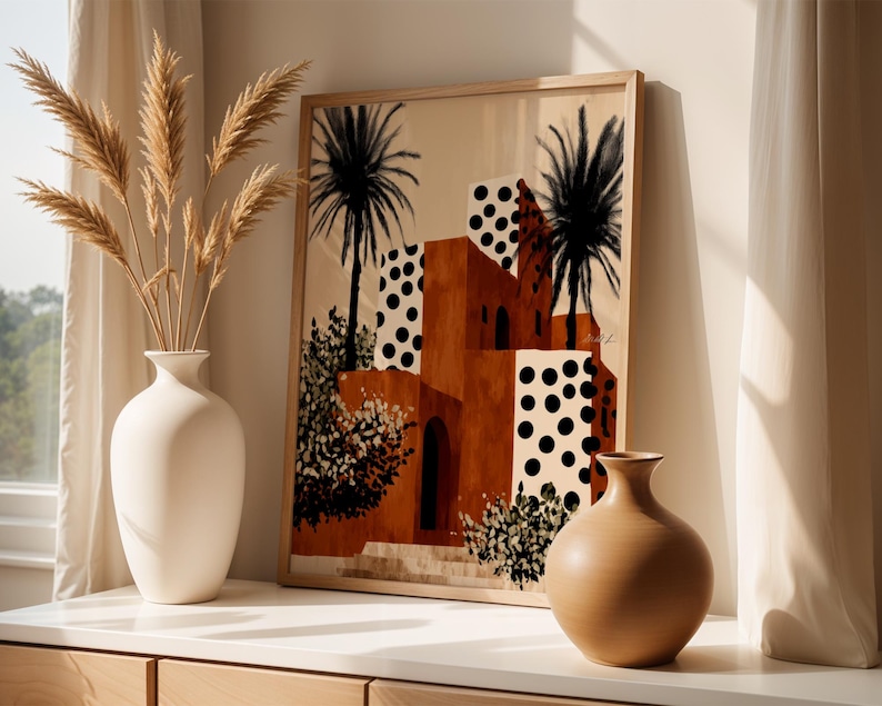 a framed painting of a desert-like scene with palm trees and buildings, placed on a shelf next to two white vases.