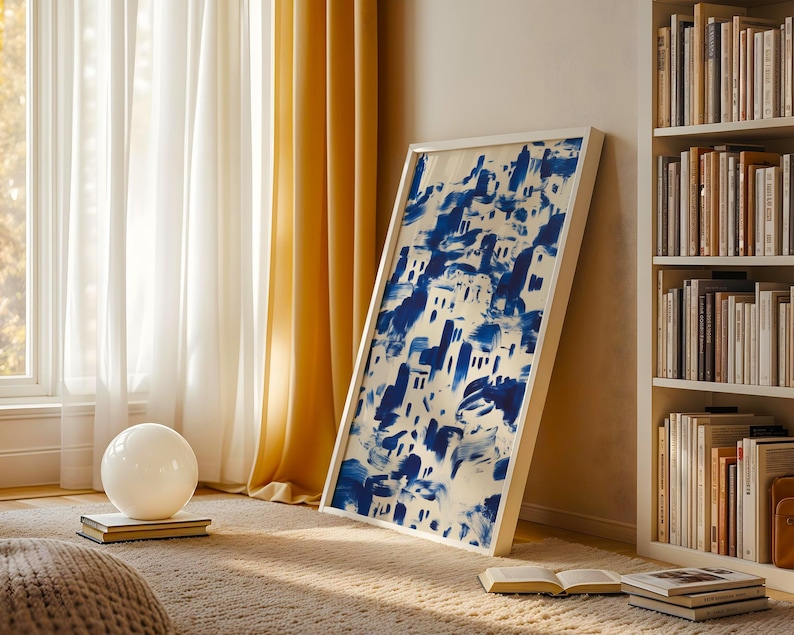 a cozy living room with a large framed painting of a blue and white abstract design hanging on the wall, a bookshelf filled with books, and a white sphere on the floor.