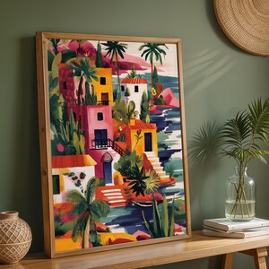 a vibrant, colorful painting of a tropical village, with buildings, palm trees, and other lush vegetation. The painting is framed and displayed on a wooden shelf, accompanied by a woven basket and a vase with a plant.