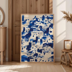 a large blue and white abstract painting displayed in a wooden frame, placed in a room with a mirror, a wooden dresser, and a small table with a vase and a candle.