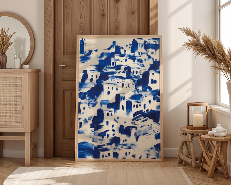 a large blue and white abstract painting displayed in a wooden frame, placed in a room with a mirror, a wooden dresser, and a small table with a vase and a candle.