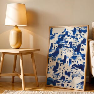 a wooden side table with a lamp on top, next to a large framed painting depicting a blue and white abstract landscape.