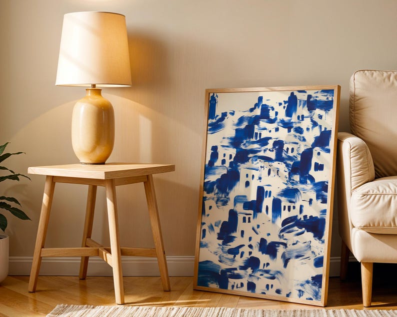 a wooden side table with a lamp on top, next to a large framed painting depicting a blue and white abstract landscape.