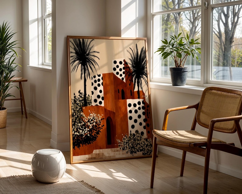a large framed painting of a desert-like landscape with palm trees and buildings, placed in a bright and sunny room with large windows.