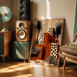 a living room with a large framed painting of a desert landscape, a brown leather armchair, a wooden side table with a lamp, and a stack of speakers.