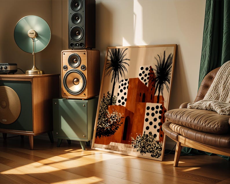 a living room with a large framed painting of a desert landscape, a brown leather armchair, a wooden side table with a lamp, and a stack of speakers.