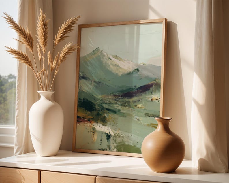 a framed landscape painting on a white shelf, accompanied by two vases. The painting depicts a mountainous scene with a mix of green, brown, and white colors. The vases are white and have a simple, elegant design. The arrangement creates a harmonious and visually appealing display.