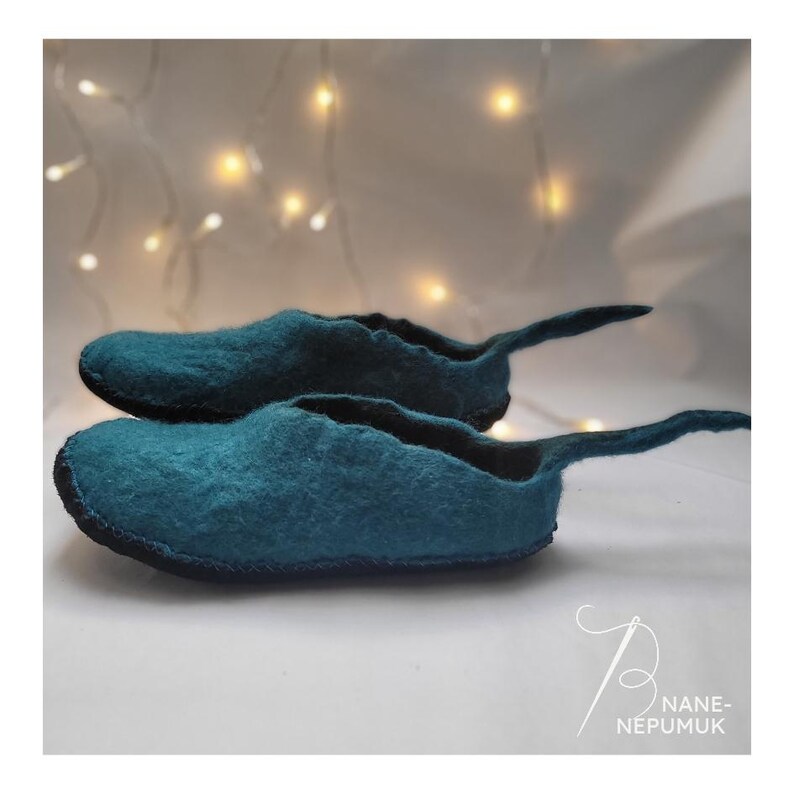K&ouml;nnte beinhalten: Zwei teal-farbene Filzschuhe mit runder Spitze und einer langen, spitz zulaufenden Verl&auml;ngerung an der Ferse. Die Schuhe sind &uuml;bereinander gestapelt, mit einem schwarzen Rand um die Sohle. Der Hintergrund ist ein weiches Wei&szlig; mit verschwommenen Lichtern.