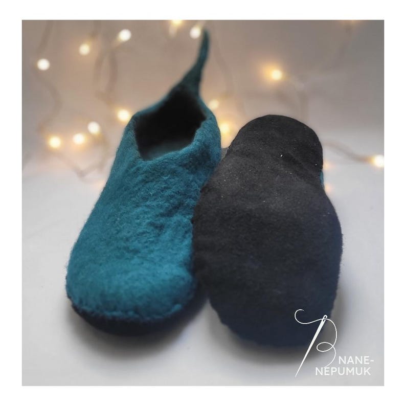 K&ouml;nnte beinhalten: Zwei Filzschuhe, einer teal und einer schwarz, werden vor einem weichen, verschwommenen Hintergrund mit kleinen, warmen Lichtern gezeigt. Der teal Schuh hat eine spitze Spitze. Der schwarze Schuh ist einfarbig. Das Bild hat einen wei&szlig;en Rand.