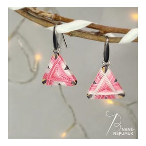 Könnte beinhalten: Handgefertigte dreieckige Ohrringe mit einem gewebten Muster aus rosa, weißen und schwarzen Fäden. Die Ohrringe hängen an silberfarbenen Ohrhaken und werden auf einem Ast präsentiert.