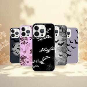 May include: Five smartphone cases with bat designs. The cases display a range of colours, including black, pink, and grey, with illustrations of bats, trees, and floral patterns. The cases are designed for a smartphone.