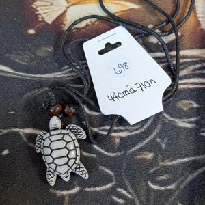 May include: A turtle pendant necklace with a black cord. The turtle pendant is white with black detailing. A white tag with the number 698 and the text "44cm 71cm" is attached to the cord.