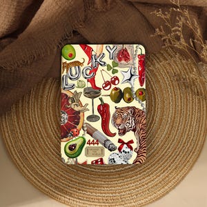 Peut inclure: Une impression rectangulaire avec le mot LUCKY en lettres ballons argentées, entouré d'illustrations d'un tigre, de piments rouges, de cerises, d'un verre à martini, d'un avocat, d'un cigare, de boules à facettes, d'une coccinelle et du texte 444 AROUND THE WORLD.
