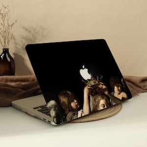 May include: A laptop skin featuring a dark background with a classical painting of three figures holding a golden crown up towards a glowing white Apple logo. The artwork depicts cherubic figures with light brown hair in a dramatic, dark setting.