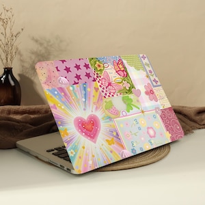 May include: A laptop skin featuring a vibrant collage design with a central pink heart surrounded by rainbow sunburst rays, butterflies, flowers, stars, and plaid patterns in shades of pink, yellow, blue, and green on a white background.