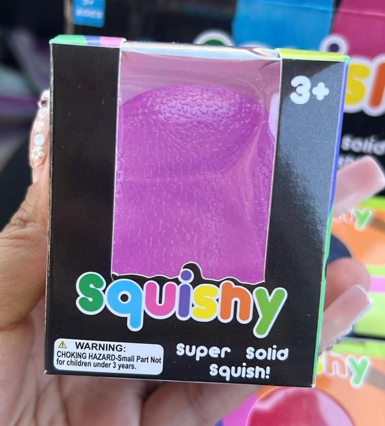 May include: A purple squishy toy in a box. The box has the word "squishy" in colourful letters. The box also has a warning label and the words "super solid squish!"