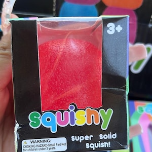 May include: A red squishy toy in a black box with the word "squishy" in colourful letters. The box also has the text "super solid squish!" and a warning about choking hazards for children under 3 years old.