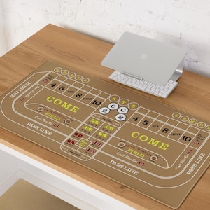 May include: A brown craps table mat with white and yellow text, including "COME", "PASS LINE", and numbers. The mat is rectangular and designed for casino-style dice games. A laptop and keyboard are on the table.