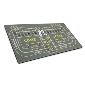 May include: A gray craps table with white and yellow text and markings. The table features areas for betting, including "COME", "PASS LINE", and numbers. Dice are placed on the table. A casino game accessory.